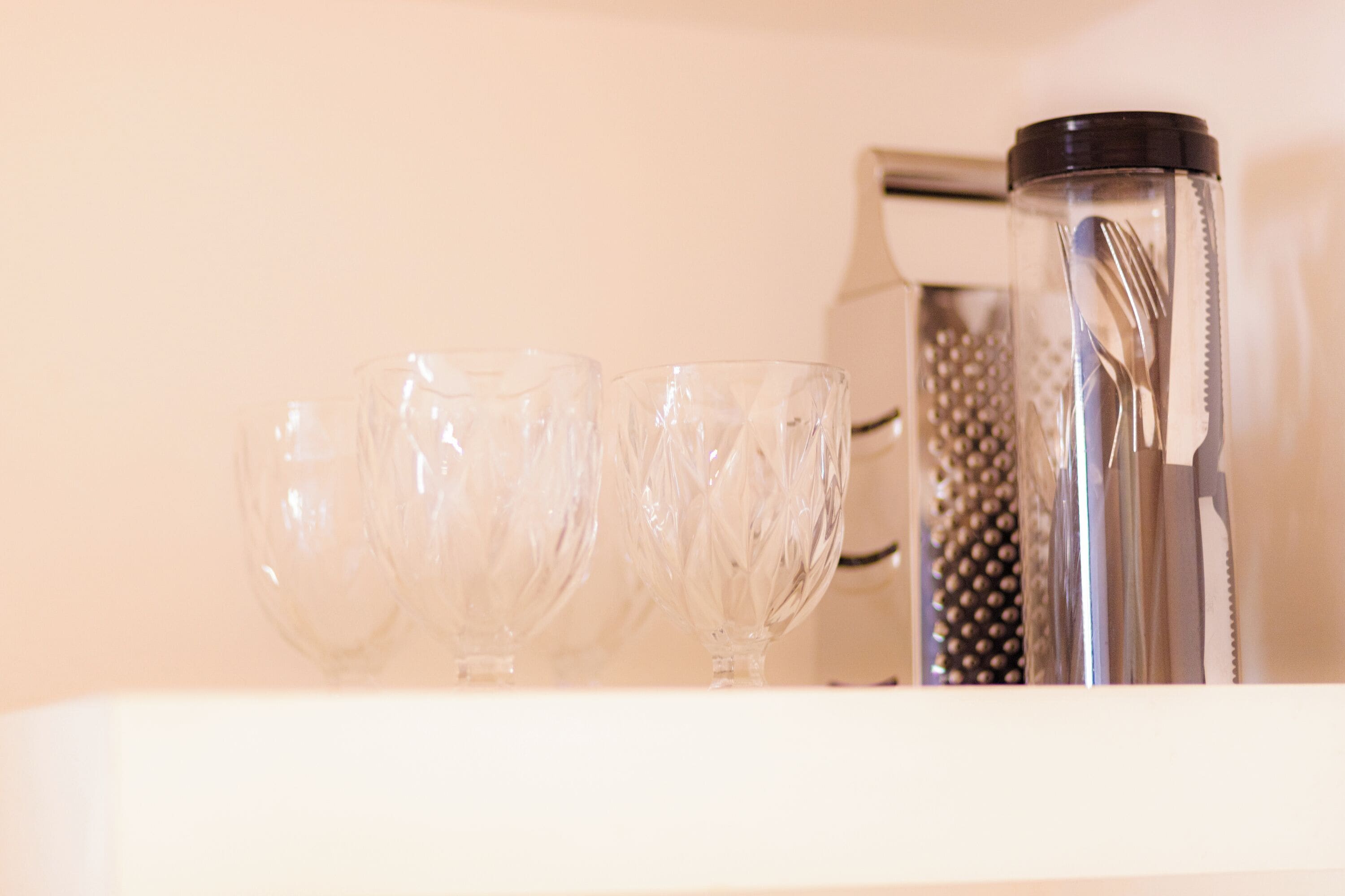 Three clear glass cups, a metal container with a lid, and a grater on a white surface.