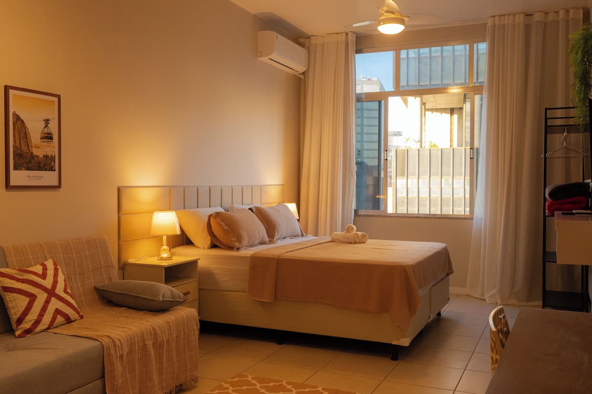 A hotel room with a bed, bedside table, lamp, and a window with curtains.