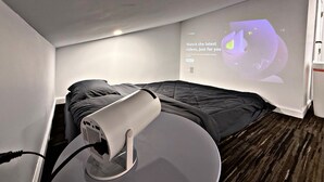 A bedroom with a bed, a projector, and a wall-mounted screen displaying a message.