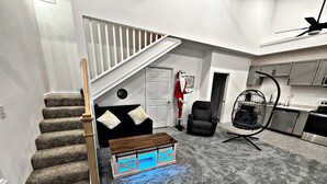 A modern interior with a staircase, a black armchair, a hanging chair, and a kitchen area.