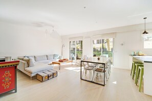 A spacious living area with a sofa, coffee table, and dining table. There is a kitchen area with a counter and stools. - Spacious apartment with outside Boulogne Roland Garros-3 bedrooms -2 bathrooms parking (Boulogne-Billancourt)