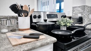 Una cocina moderna con estufa de acero inoxidable, una olla en la estufa, tabla de cortar con cuchillos y una planta en la encimera.