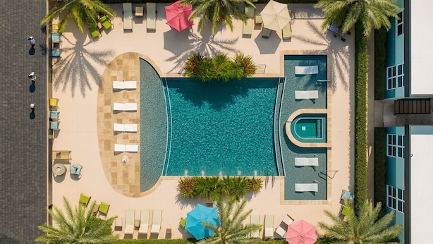 Vista aérea de un resort con piscina central, tumbonas y palmeras.