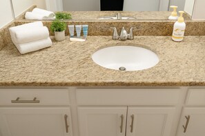 A bathroom with a granite countertop, a white sink, a mirror, a potted plant, a towel rack, and a soap dispenser. - Houston 2BR Resort‑Style, Pool Gym Patio & Parking (Houston)