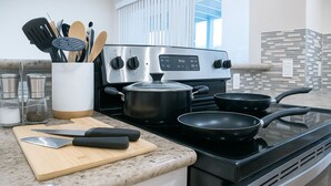 A modern kitchen with a stainless steel stove, a wooden cutting board, a knife, and a pot. - Houston 2BR Resort‑Style, Pool Gym Patio & Parking (Houston)