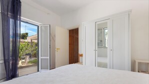 Ein Schlafzimmer mit einem großen Bett, einer Glastür zum Außenbereich und einer Holztür zu einem Kleiderschrank.