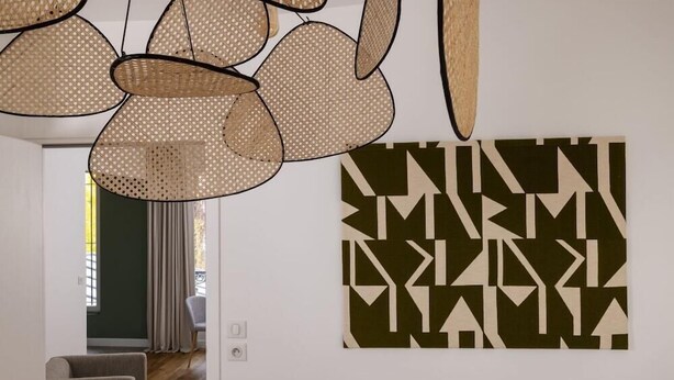 Et moderne interiør med et geometrisk kunstværk på væggen og en vævet lampe.