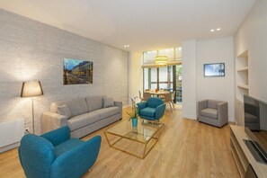 A modern living room with a grey sofa, blue armchairs, a glass coffee table, a lamp, and a fireplace. - Yuna Blanche Serviced Apartments (Paris)