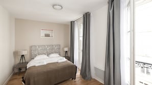 Et soveværelse med en seng, to sengeborde, en lampe, et billede på væggen og et vindue med gardiner.