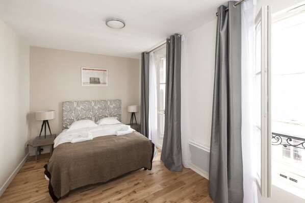 A bedroom with a bed, two bedside tables, a lamp, a picture on the wall, and a window with curtains. - Yuna Blanche Serviced Apartments (Paris)