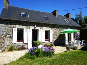 A stone house with a gravel driveway, a garden with purple flowers, and a green umbrella. - Charming Breton House Near Petit Havre Beach (Pordic)