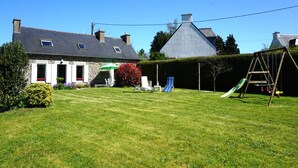 A house with a stone facade, a green lawn, a swing set, and a clear blue sky. - Charming Breton House Near Petit Havre Beach (Pordic)