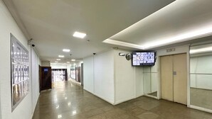 Un pasillo limpio y bien iluminado con suelo de baldosas, un televisor montado y una cámara de seguridad.