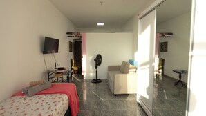 Una habitación con cama, sofá, televisión, ventilador y mesa.