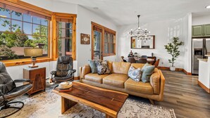 A spacious living room with a leather sofa, wooden coffee table, and a large window with a view of greenery.