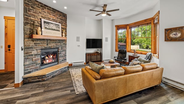 A living room with a stone fireplace, leather sofa, and a large window with a view of greenery.