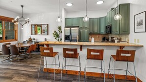 A modern kitchen with green cabinets, a central island with bar stools, and pendant lighting.