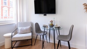 A modern living room with a flat-screen TV mounted on the wall, a round glass table with two chairs, a small white table, and a window with curtains. - Apartment in Koblenz Near Deutsches Eck (Koblenz)