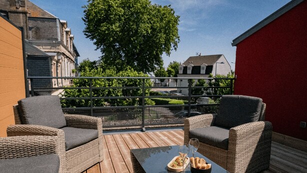 Ein Balkon mit Korbmöbeln, einem Glastisch und Blick auf Gebäude und Bäume.