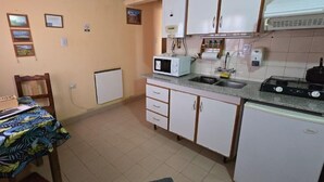 Een kleine keuken met witte kasten, een magnetron, een broodrooster en een spoelbak.