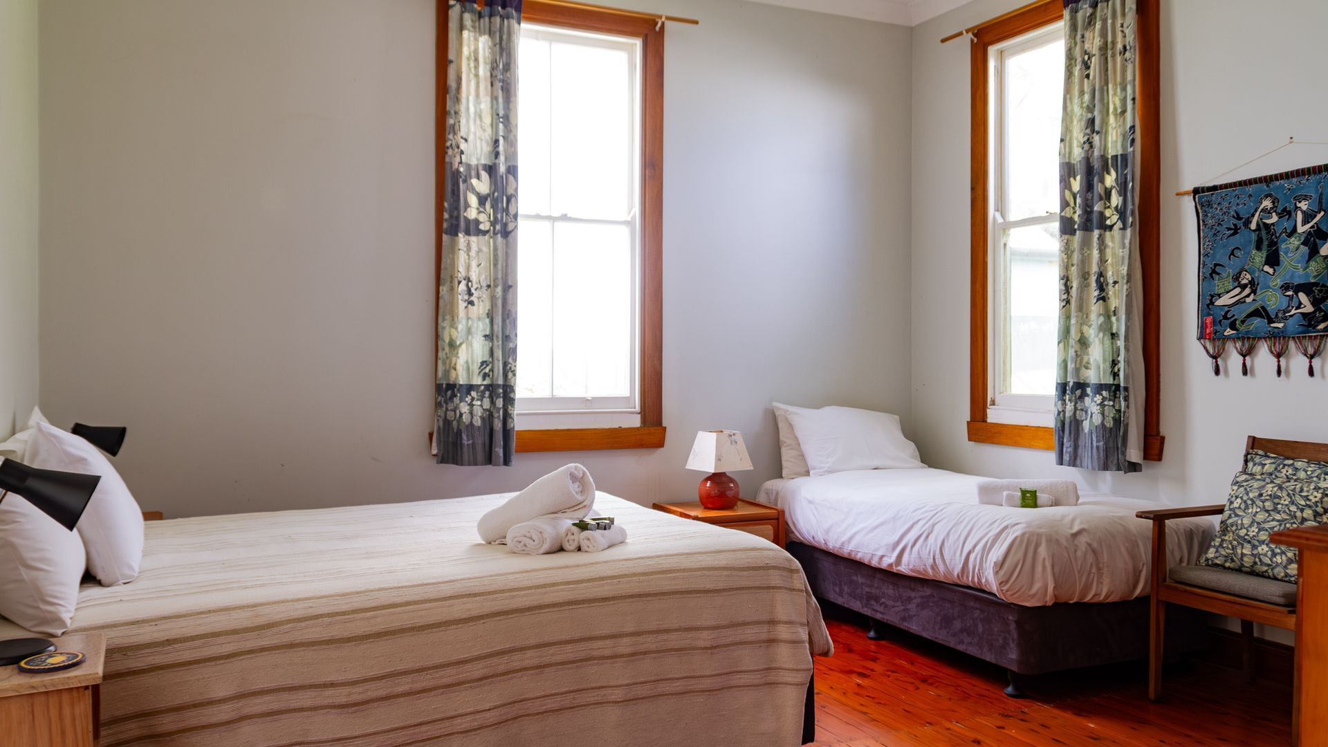 Habitación de hotel con dos camas, suelo de madera y cortinas estampadas.