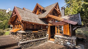 A log cabin with a stone foundation, wooden deck, and a chimney.