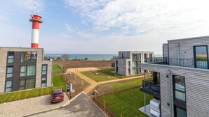 A modern building with a red and white tower, a parking area, and a view of the sea.