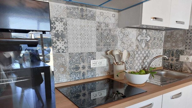 A modern kitchen with patterned backsplash tiles, stainless steel appliances, and wooden countertops.