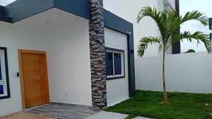 A modern building with a wooden door, stone pillar, and a small palm tree in the yard. - Charming 2-bedroom villa in lovely Punta Cana with AC, WiFi (Punta Cana)