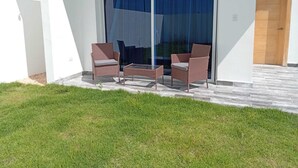 A modern outdoor seating area with wicker chairs and a glass table, adjacent to a sliding glass door leading to a covered patio. - Charming 2-bedroom villa in lovely Punta Cana with AC, WiFi (Punta Cana)