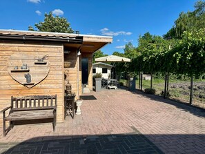 En rustik träbyggnad med en hylla i form av ett hjärta där dekorativa föremål visas upp, en innergård med ett stengolv och en pergola med ett parasoll.