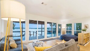 A spacious living room with a large window overlooking a deck and water, a sofa, a coffee table, and a lamp. - Family Cove Retreat - newly remodeled! (Point Blank)