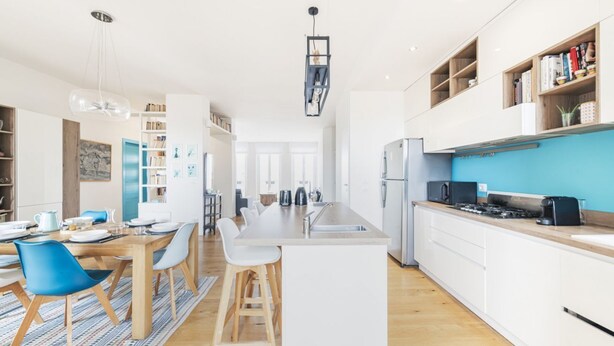 Een moderne keuken met een centraal kookeiland, witte kasten en een blauwe accentmuur.