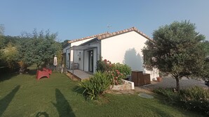 Una casa de una planta con fachada blanca y techo marrón, rodeada de un césped cuidado y diversas plantas.