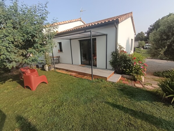 Een modern huis met terras, een rode plastic stoel en een tuin met diverse planten.