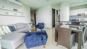 Una sala de estar moderna con un sofá gris, un sillón azul y un comedor con sillas de mimbre y una mesa blanca.
