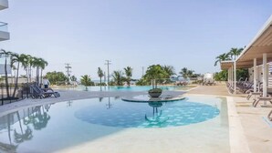 Una piscina con diseño circular, rodeada de sillas de descanso y palmeras.