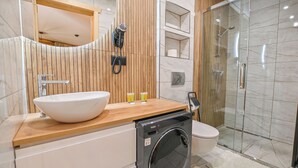 Een moderne badkamer met een groot wastafel, toilet, douchecabine van glas en een ingebouwde wasmachine.