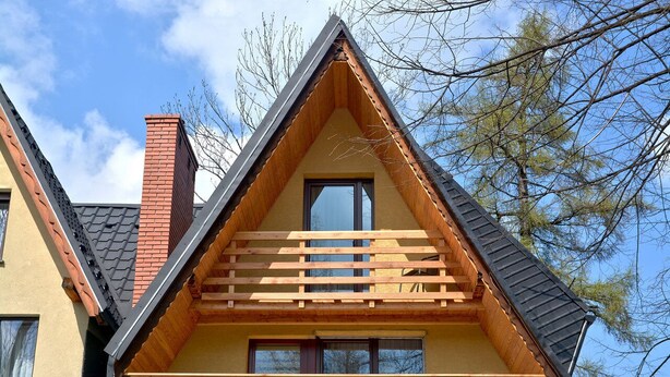 Eine dreieckige Holzhütte mit Balkon, Fenster und Schornstein.