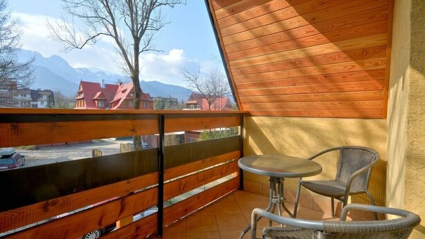 Een balkon met een houten leuning, een tafel en twee rieten stoelen.