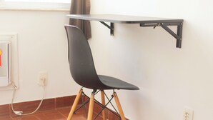 A chair with a black seat and backrest, wooden legs, and a metal frame, positioned in front of a white wall with a window and a power outlet. - SUH Catete 02 Christ View (Rio de Janeiro)