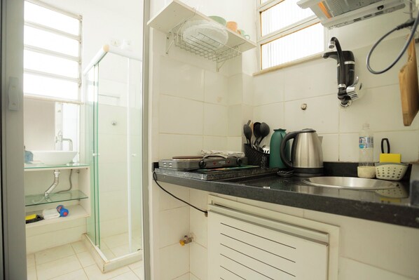 A kitchen with a glass shower enclosure, a sink, and a countertop with various appliances and utensils.