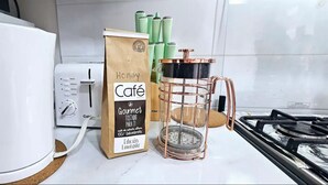 Una cocina con una cafetera blanca, una bolsa de café gourmet, un termo verde y una cafetera de cobre sobre la encimera.