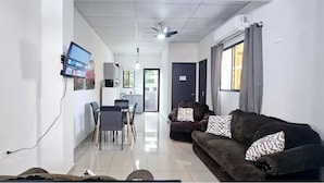 Una sala de estar moderna con un sofá, un televisor montado en la pared y un comedor con sillas y una mesa.