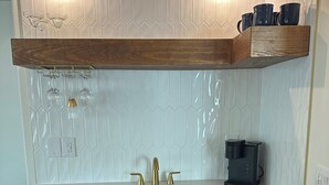 A kitchen with a white countertop, a built-in dishwasher, a coffee maker, and a wooden shelf above the sink. - Peaceful Retreat w/ Trail Access and Convenience (Bella Vista)