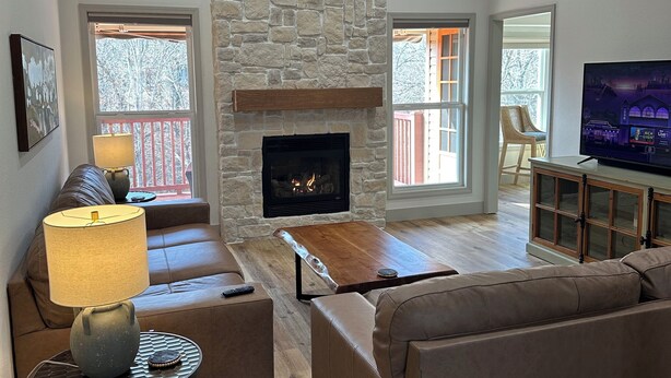 A living room with a stone fireplace, leather sofas, a coffee table, and a television on a cabinet. - Peaceful Retreat w/ Trail Access and Convenience (Bella Vista)