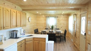 Interior de una cabaña de madera con cocina, comedor y una puerta visible.