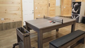 Una habitación con mesa de ping pong, un banco y un refrigerador con una imagen de vaca.
