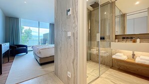 A modern hotel room with a large bed, a desk, a chair, a glass-enclosed shower, and a bathroom with a large mirror and toiletries. - Monumental Sea Sky by Atlantic Holiday (Funchal)
