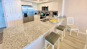 Una cocina moderna con encimeras de granito, electrodomésticos de acero inoxidable y muebles de cocina blancos.